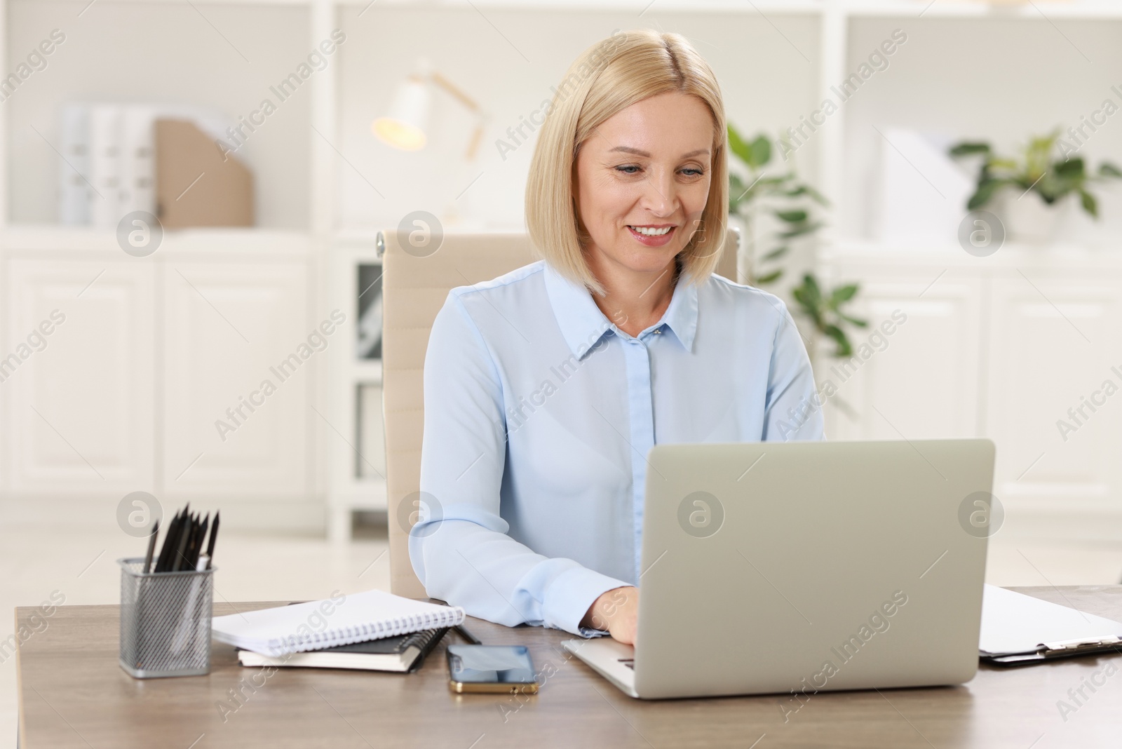 Photo of Smiling middle aged woman working with laptop at table in office