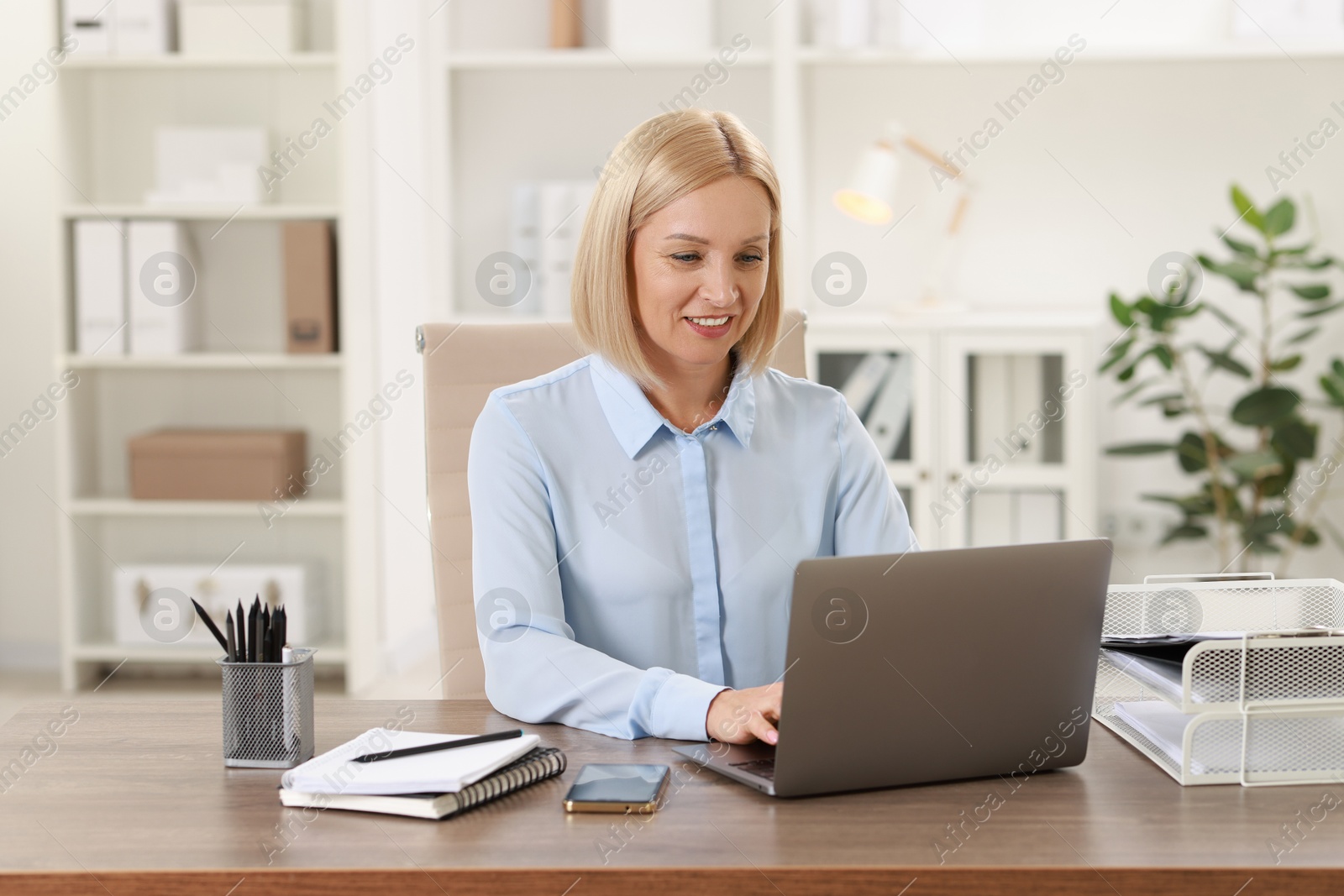 Photo of Smiling middle aged woman working with laptop at table in office