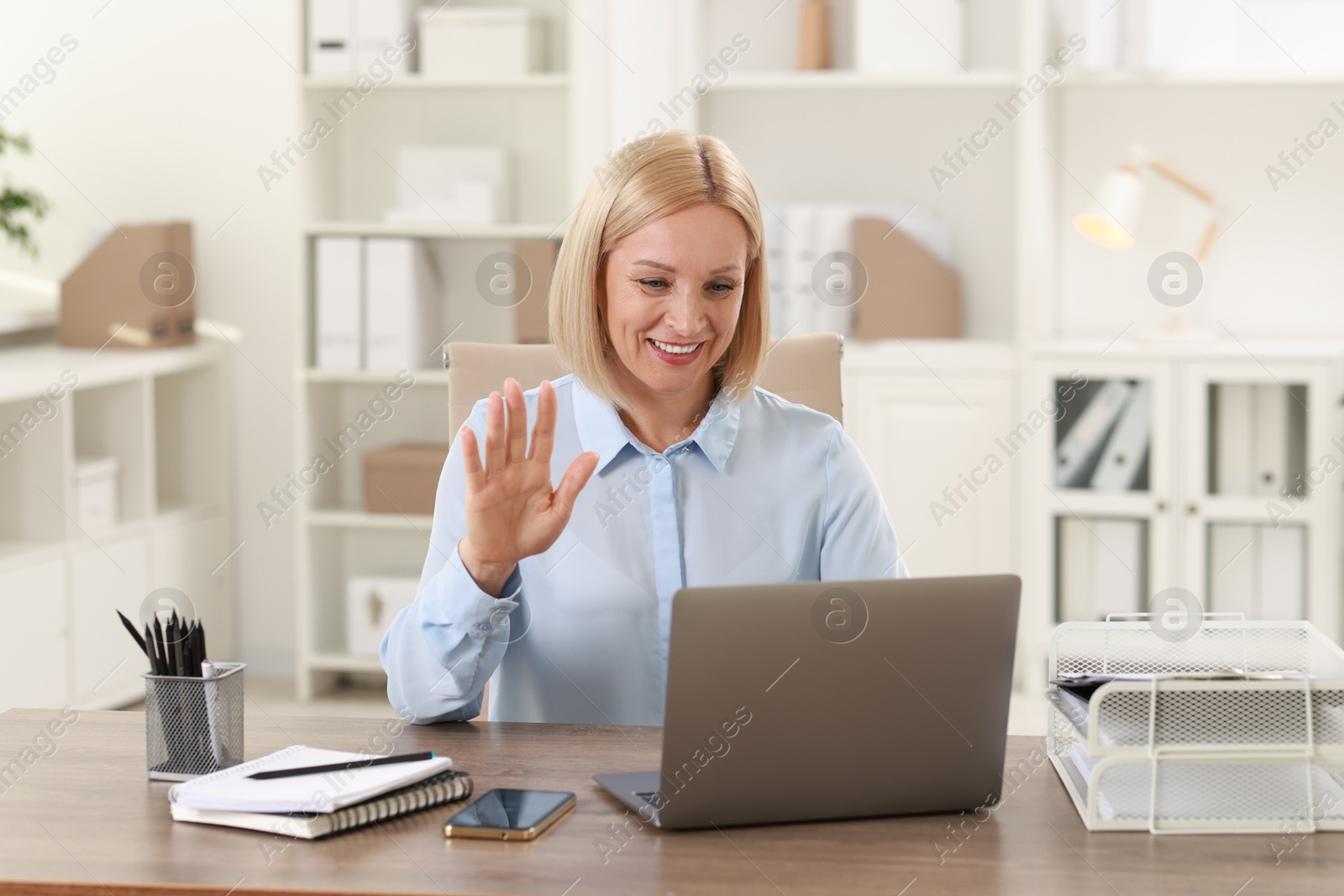 Photo of Smiling middle aged woman having videochat by laptop at table in office