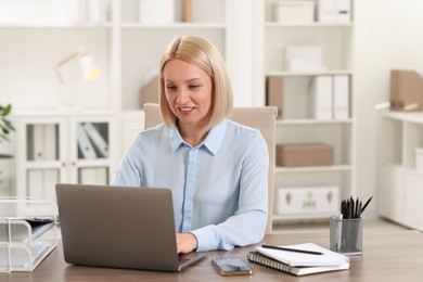 Photo of Smiling middle aged woman working with laptop at table in office