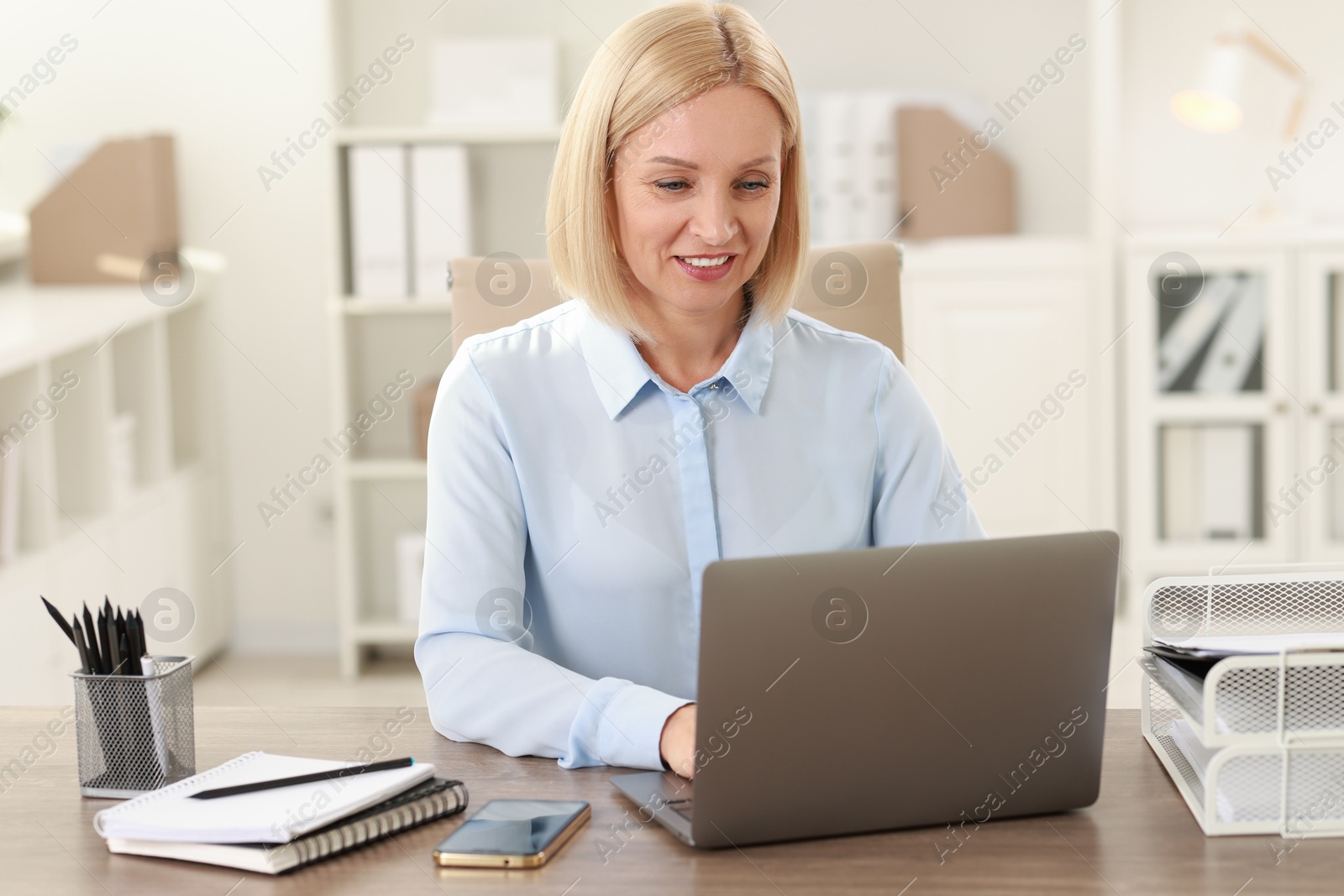 Photo of Smiling middle aged woman working with laptop at table in office