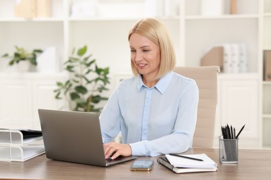 Photo of Smiling middle aged woman working with laptop at table in office