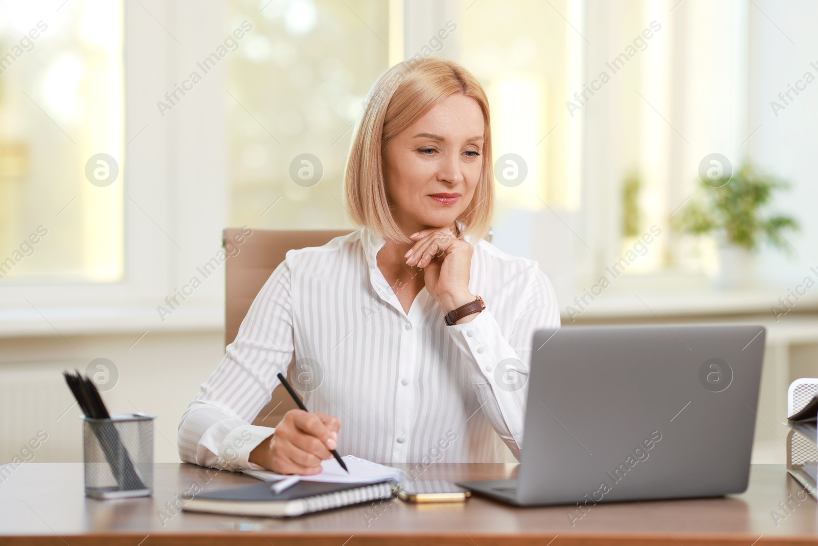 Photo of Middle aged woman working with laptop at table in office