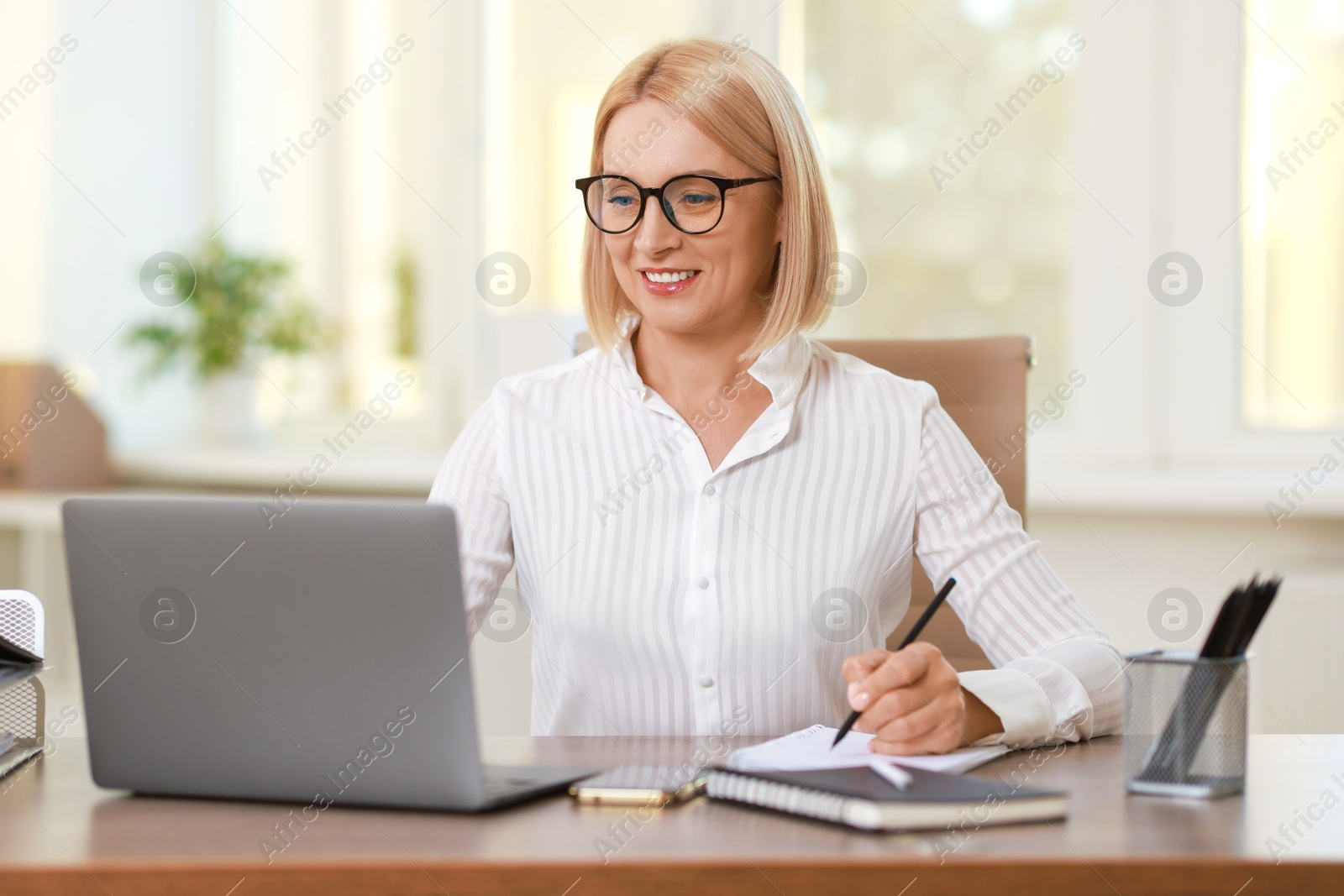 Photo of Smiling middle aged woman working with laptop at table in office