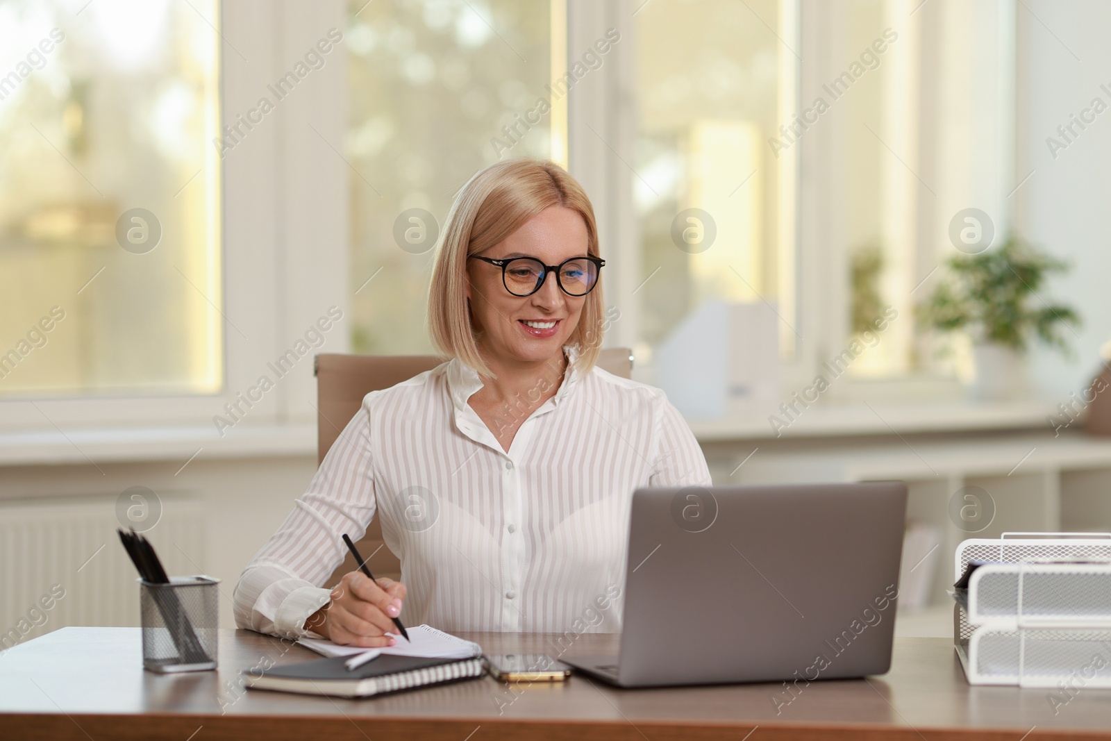 Photo of Smiling middle aged woman working with laptop at table in office