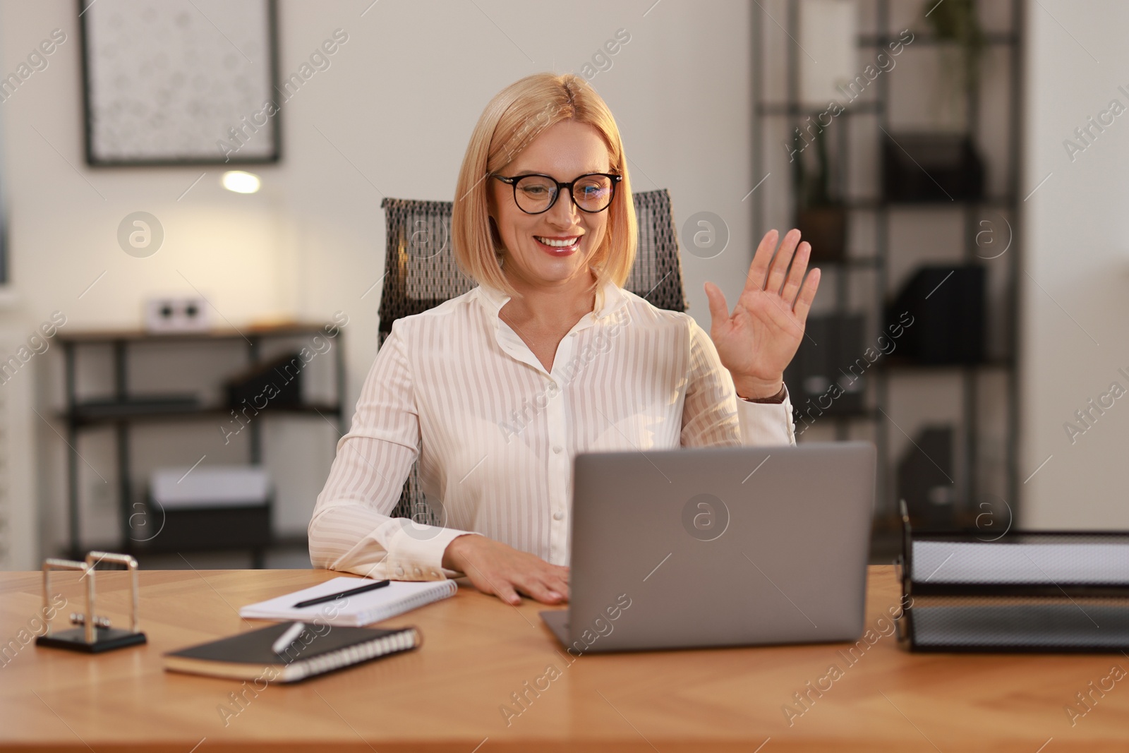 Photo of Smiling middle aged woman having videochat by laptop at table in office