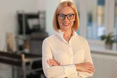 Photo of Portrait of smiling middle aged woman with crossed arms in office. Space for text