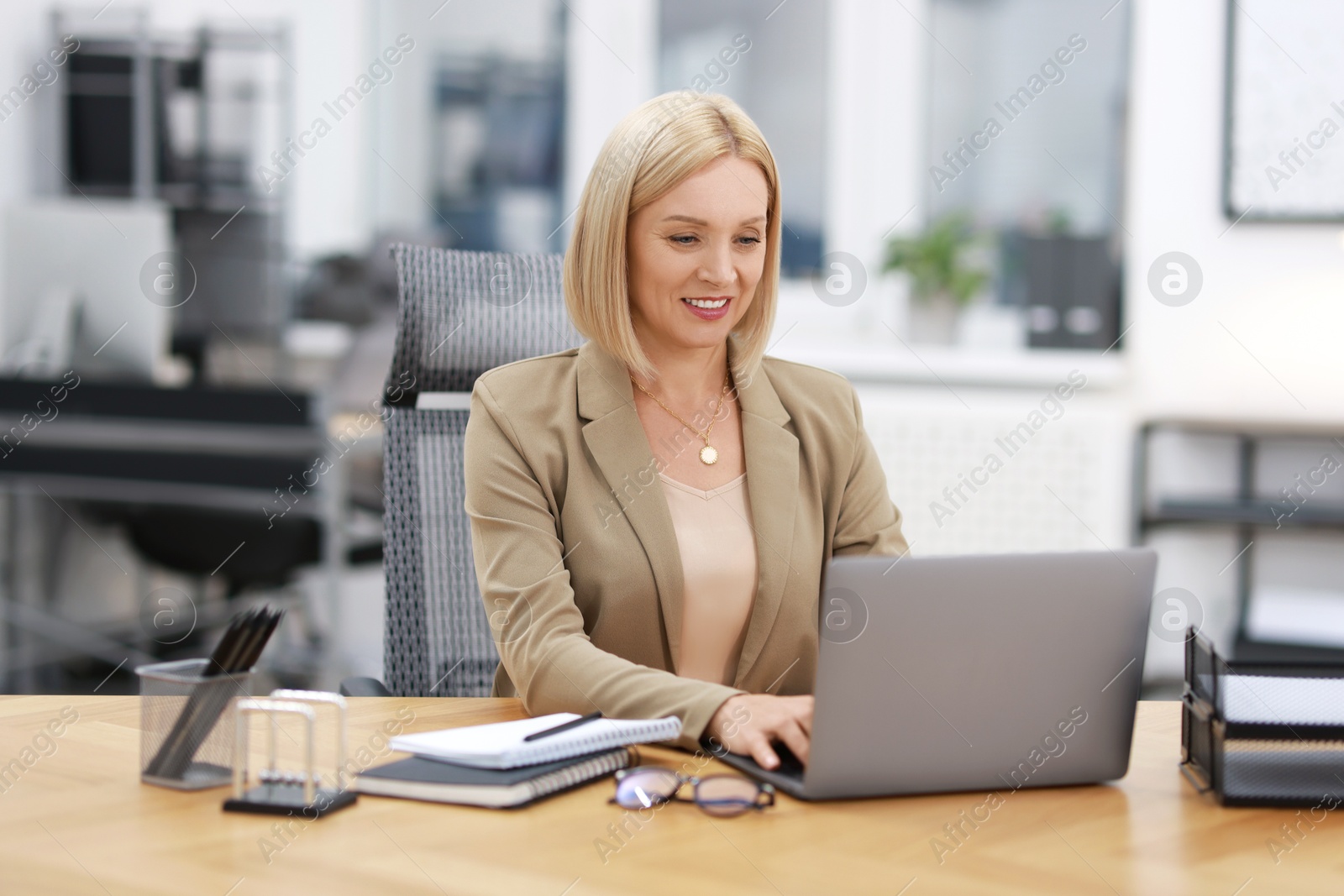 Photo of Smiling middle aged woman working with laptop at table in office