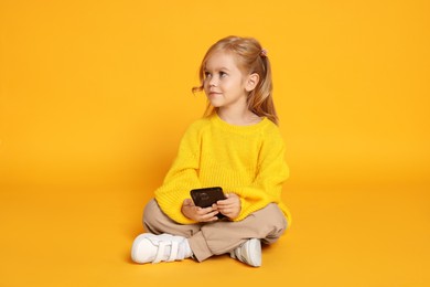 Photo of Cute little girl with smartphone against orange background