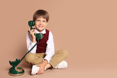 Photo of Cute little boy with old telephone on beige background, space for text