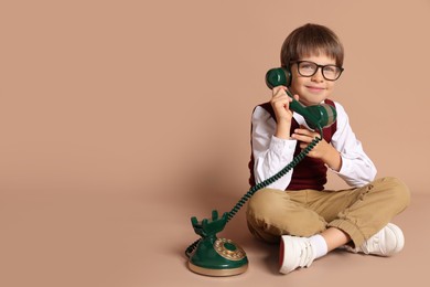 Photo of Cute little boy with old telephone on beige background, space for text