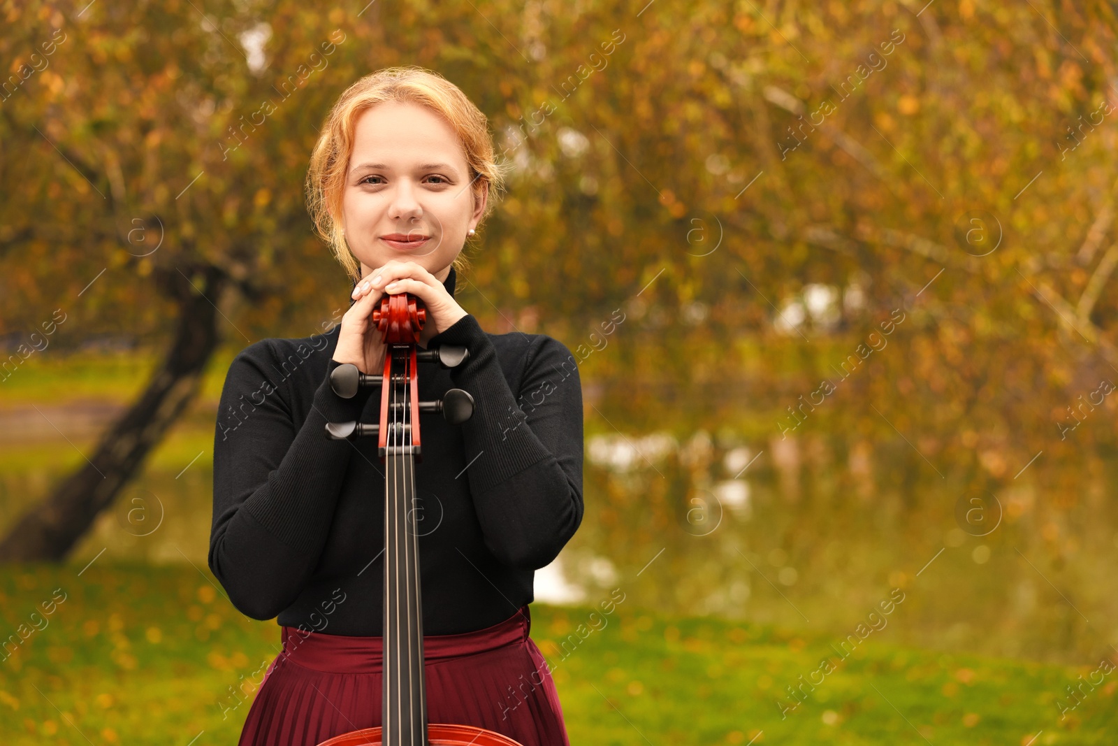 Photo of Beautiful young woman with cello in park, space for text