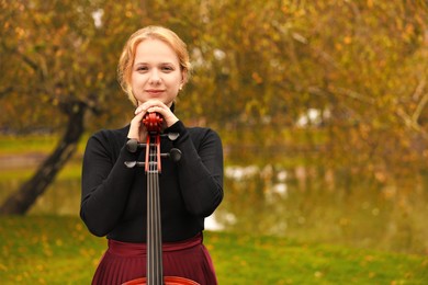 Photo of Beautiful young woman with cello in park, space for text