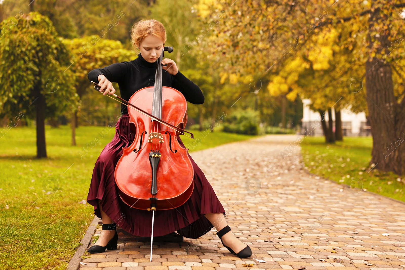 Photo of Beautiful young woman playing cello in park, space for text