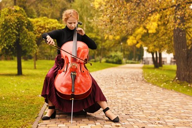 Beautiful young woman playing cello in park, space for text