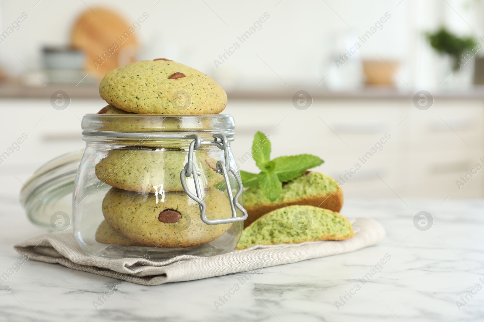 Photo of Delicious mint chocolate chip cookies in jar on white marble table, closeup. Space for text