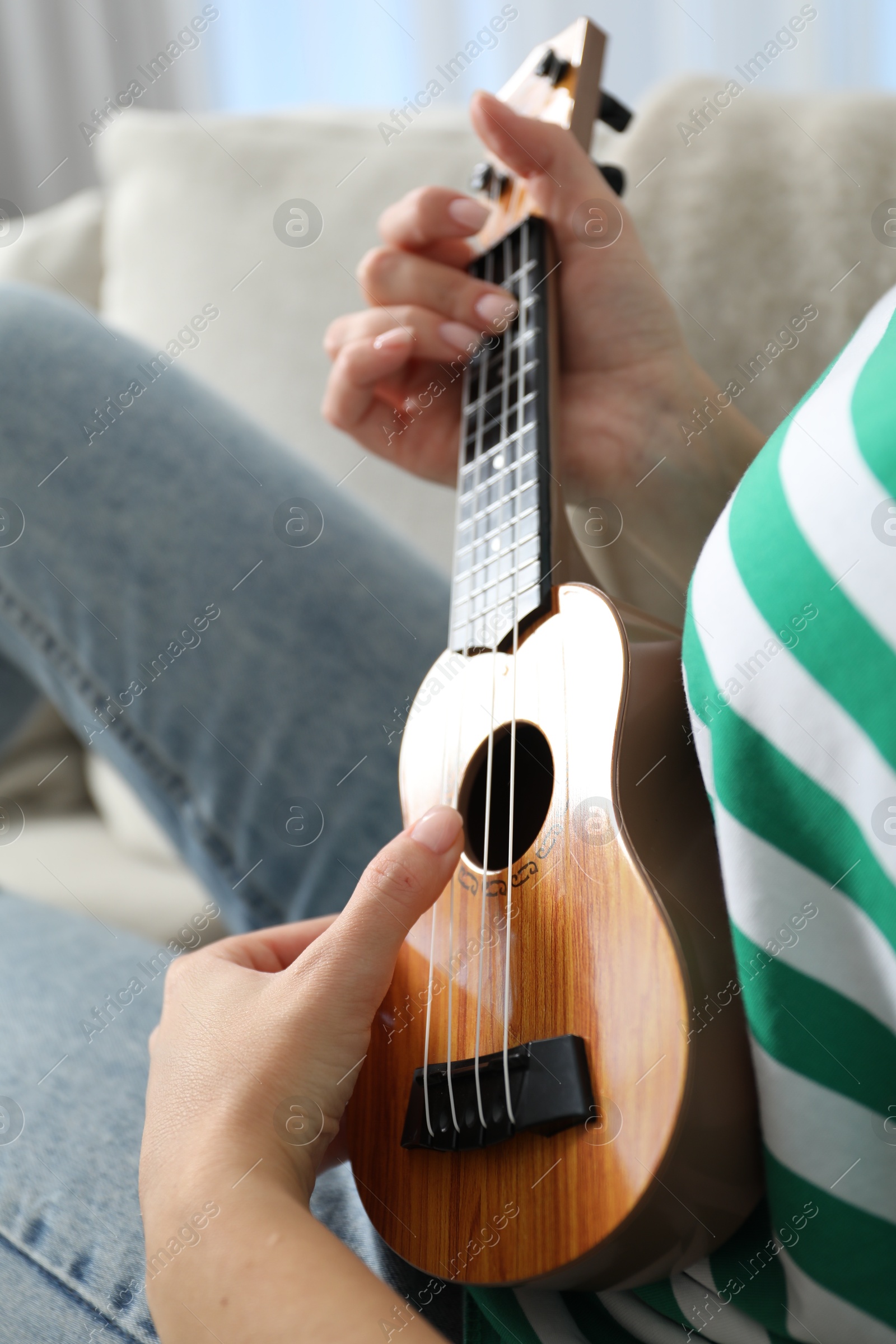 Photo of Woman playing ukulele on sofa at home, closeup