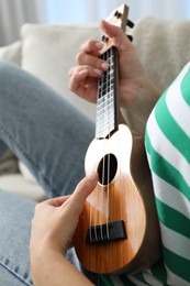 Photo of Woman playing ukulele on sofa at home, closeup