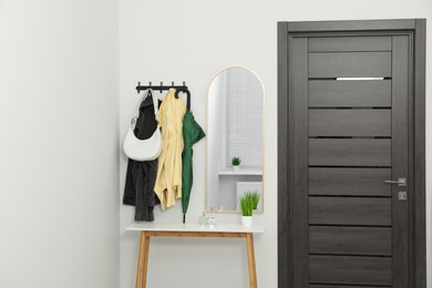 Photo of Mirror, rack with clothes and shoe storage bench in hallway. Interior design