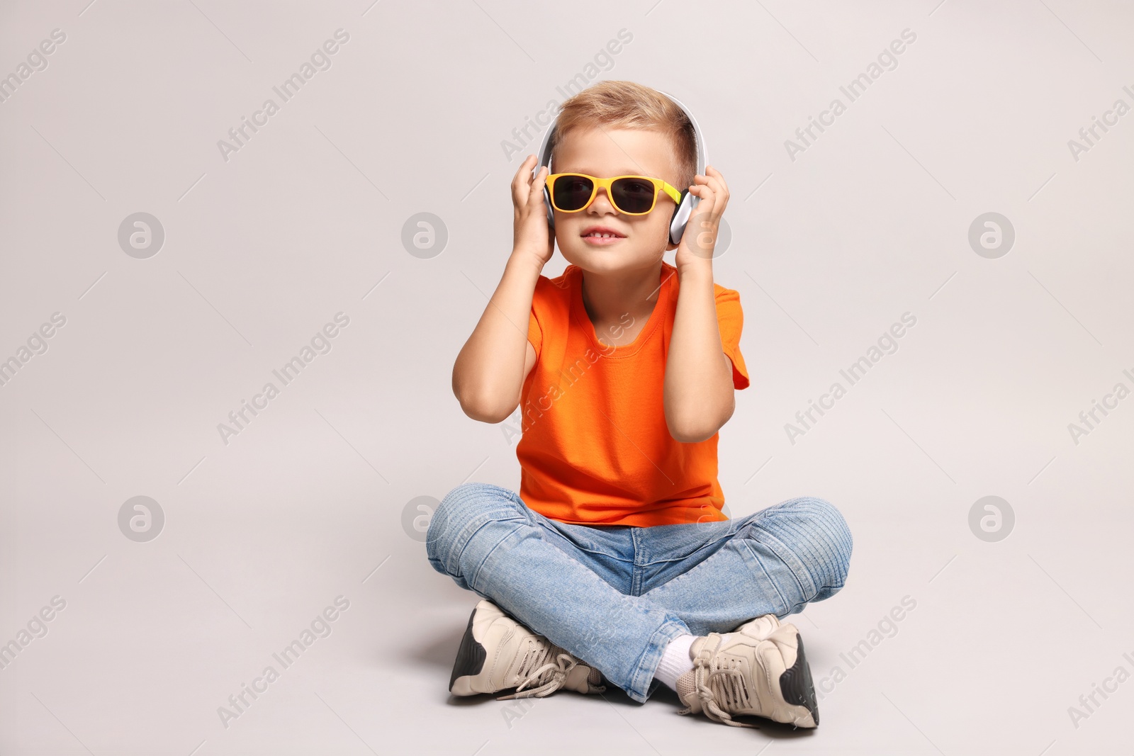 Photo of Little boy with sunglasses listening to music on light grey background