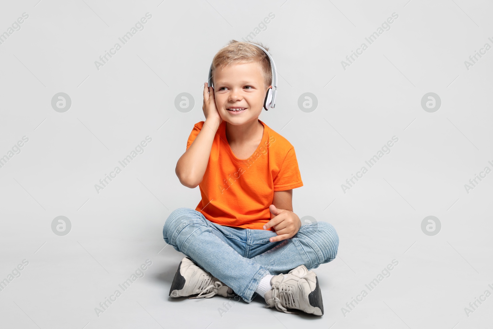 Photo of Little boy listening to music and showing rock gesture on light grey background