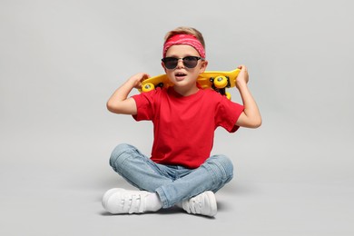 Little boy with sunglasses and skateboard on light grey background