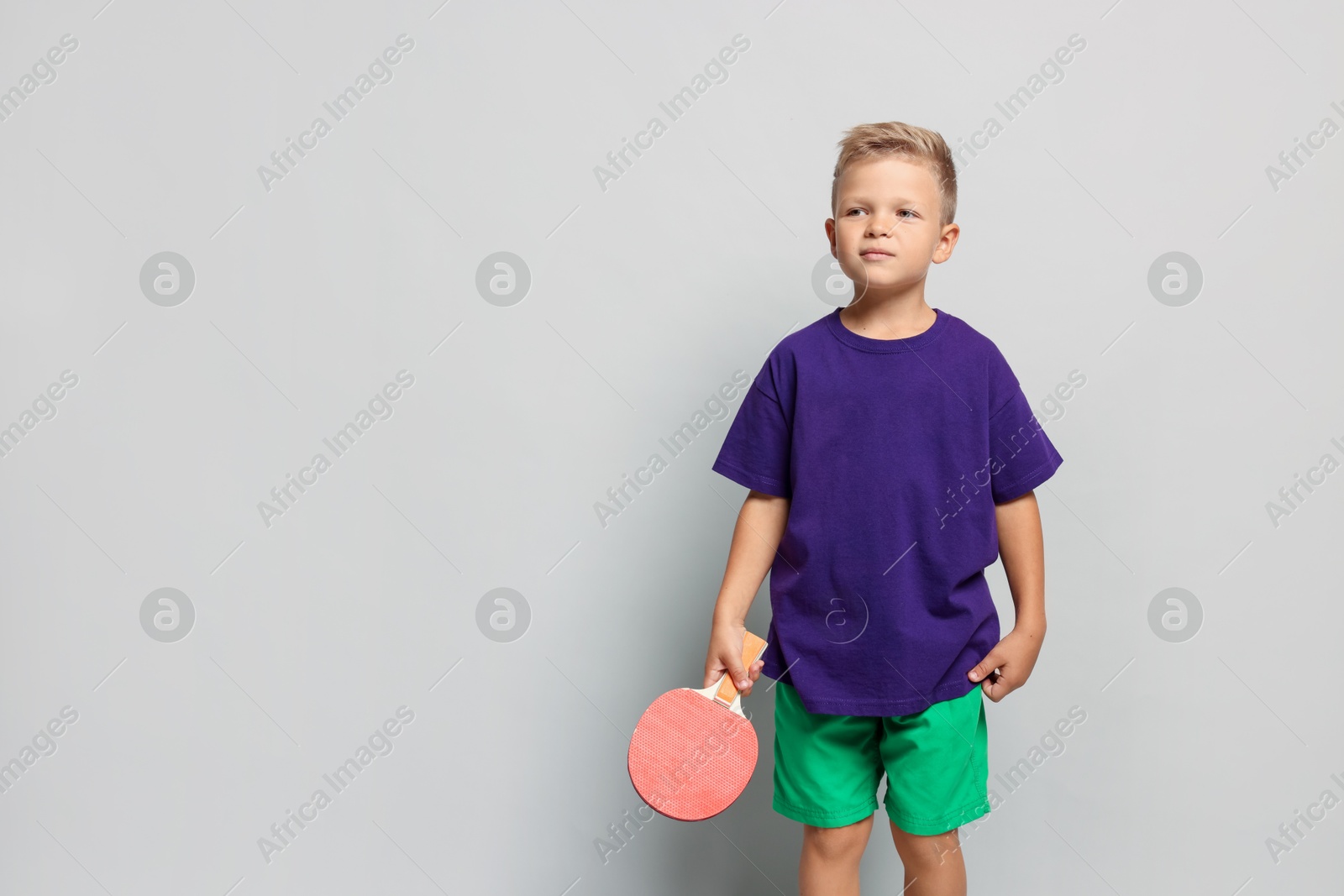 Photo of Little boy with ping pong racket on light grey background, space for text