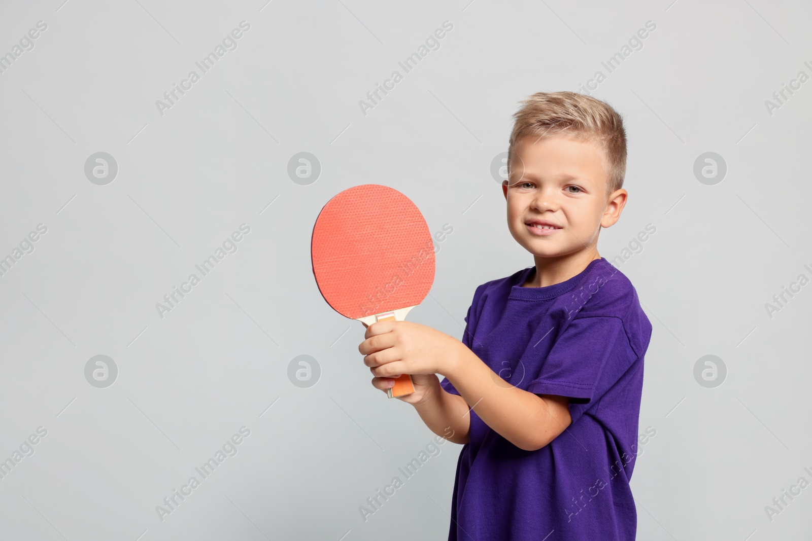 Photo of Little boy with ping pong racket on light grey background, space for text