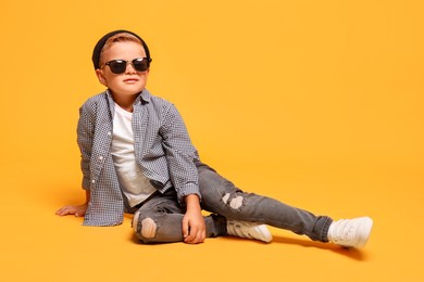 Little boy with stylish clothes and sunglasses on orange background