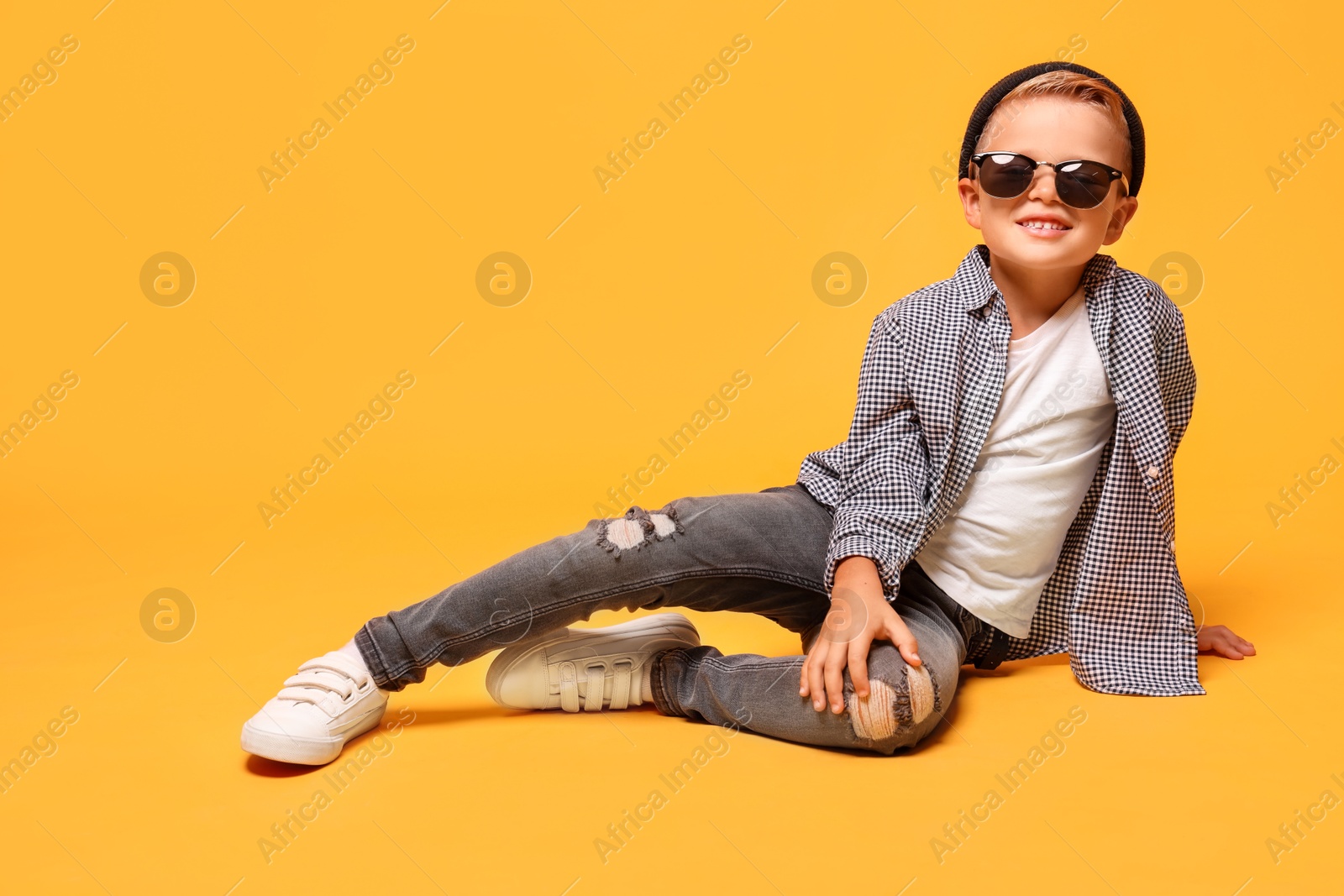 Photo of Little boy with stylish clothes and sunglasses on orange background