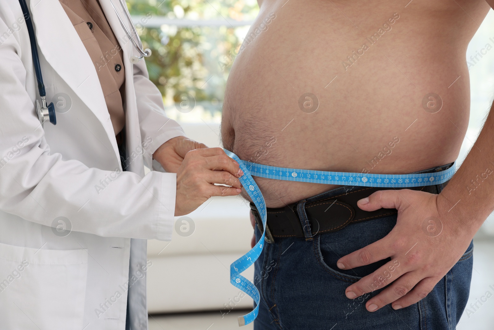 Photo of Nutritionist measuring overweight man's waist with tape in clinic, closeup