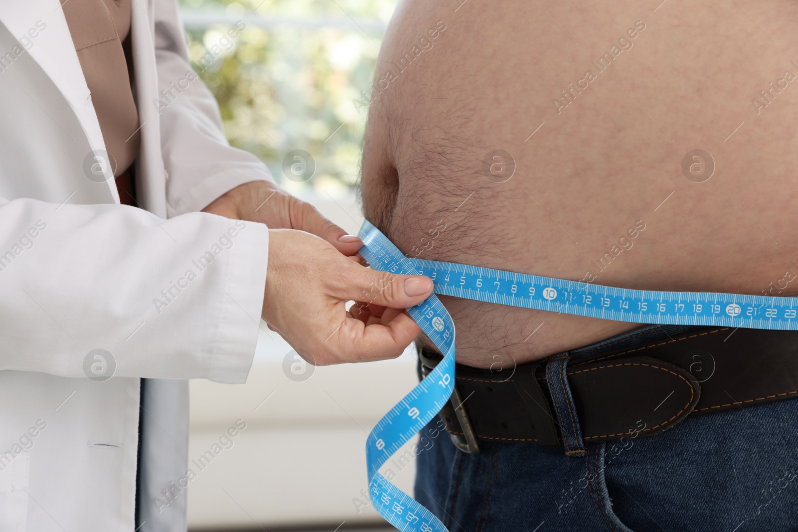 Photo of Nutritionist measuring overweight man's waist with tape in clinic, closeup