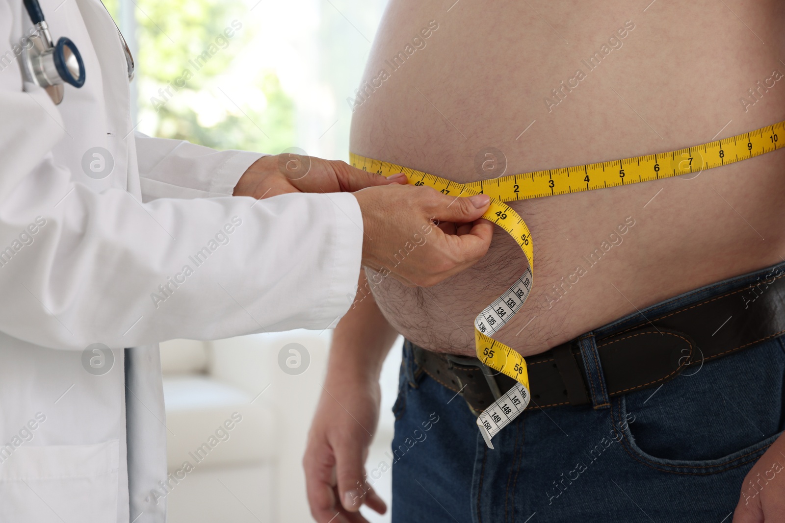 Photo of Nutritionist measuring overweight man's waist with tape in clinic, closeup