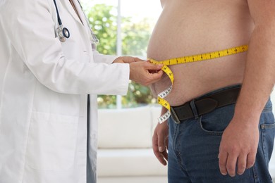 Photo of Nutritionist measuring overweight man's waist with tape in clinic, closeup