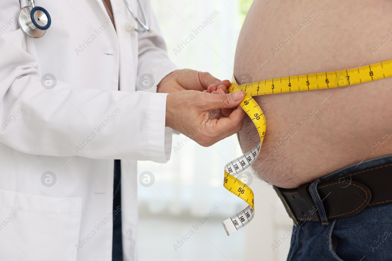 Photo of Nutritionist measuring overweight man's waist with tape in clinic, closeup