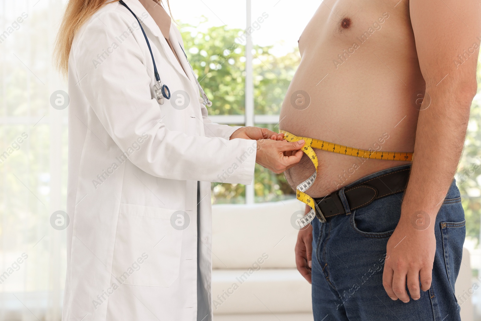 Photo of Nutritionist measuring overweight man's waist with tape in clinic, closeup