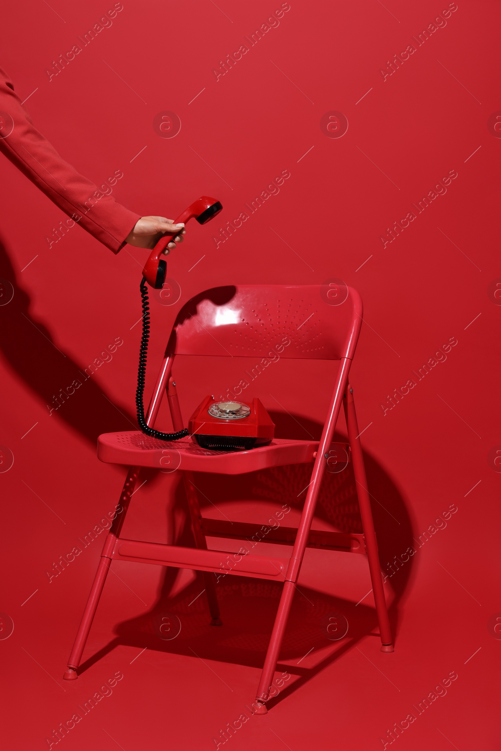 Photo of Woman with corded telephone on chair against red background, closeup