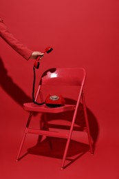 Photo of Woman with corded telephone on chair against red background, closeup