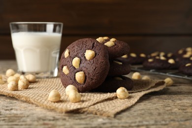 Photo of Tasty chocolate cookies with hazelnuts and milk on wooden table, closeup