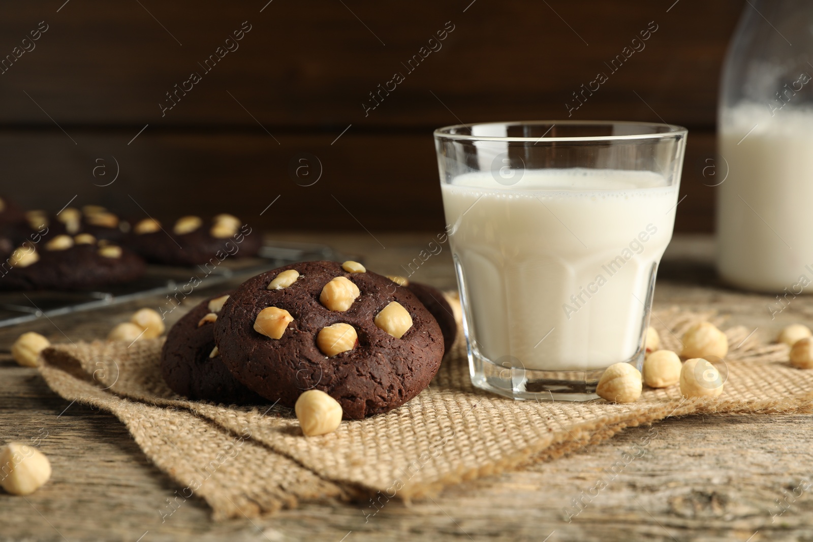 Photo of Tasty chocolate cookies with hazelnuts and milk on wooden table, closeup