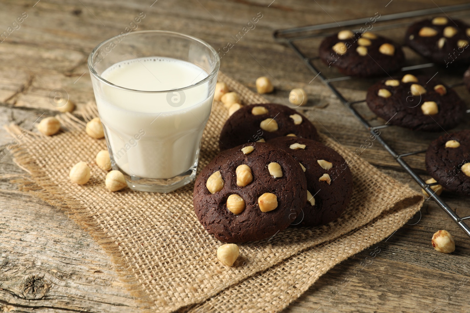 Photo of Tasty chocolate cookies with hazelnuts and milk on wooden table, closeup