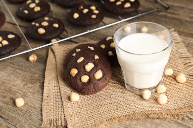 Photo of Tasty chocolate cookies with hazelnuts and milk on wooden table, closeup