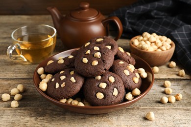 Photo of Tasty chocolate cookies with hazelnuts and tea on wooden table, closeup