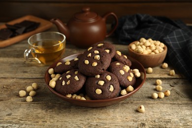 Photo of Tasty chocolate cookies with hazelnuts and tea on wooden table