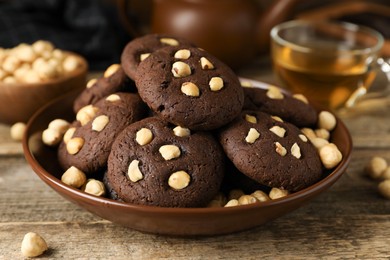 Photo of Tasty chocolate cookies with hazelnuts and tea on wooden table, closeup