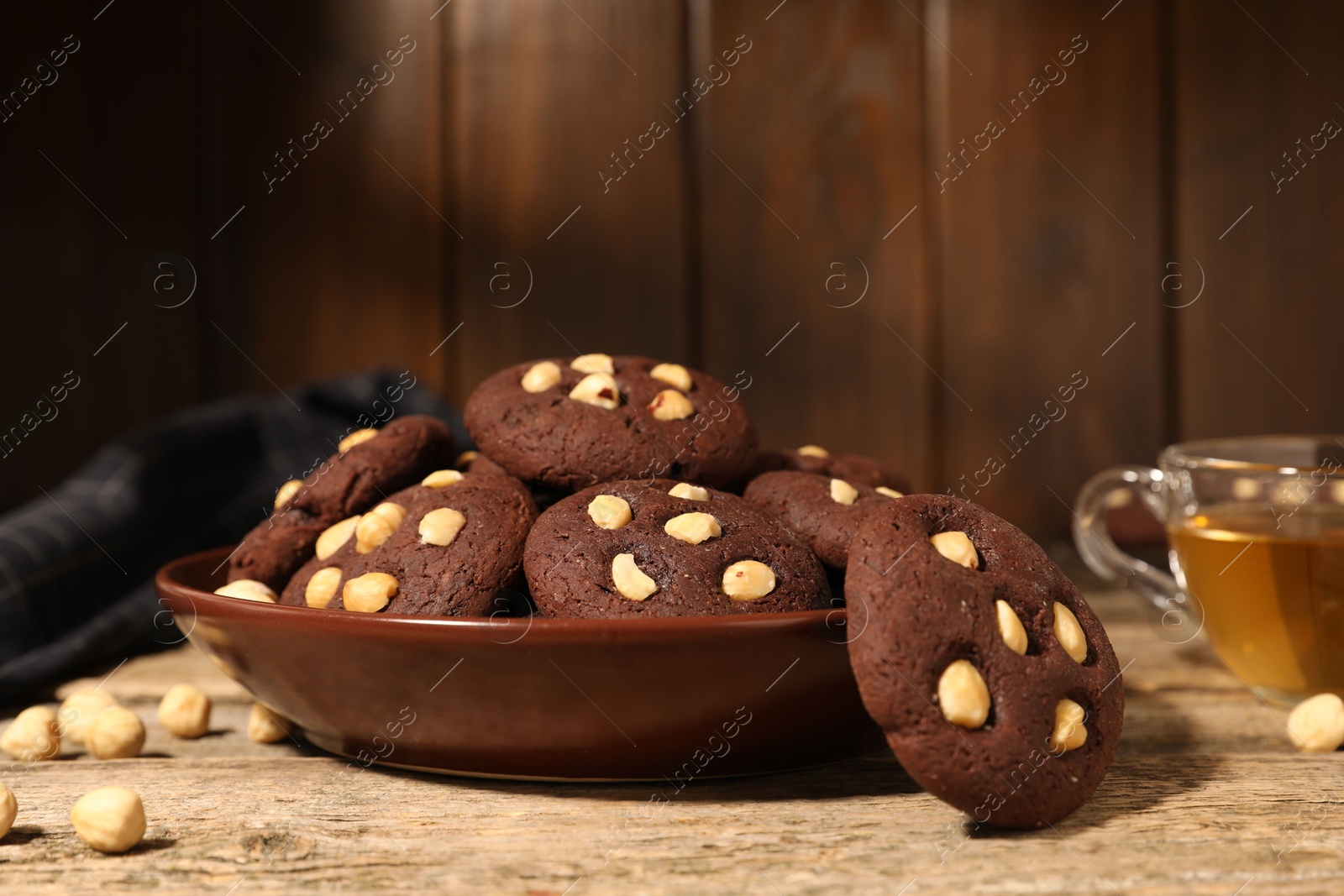 Photo of Tasty chocolate cookies with hazelnuts and tea on wooden table, closeup