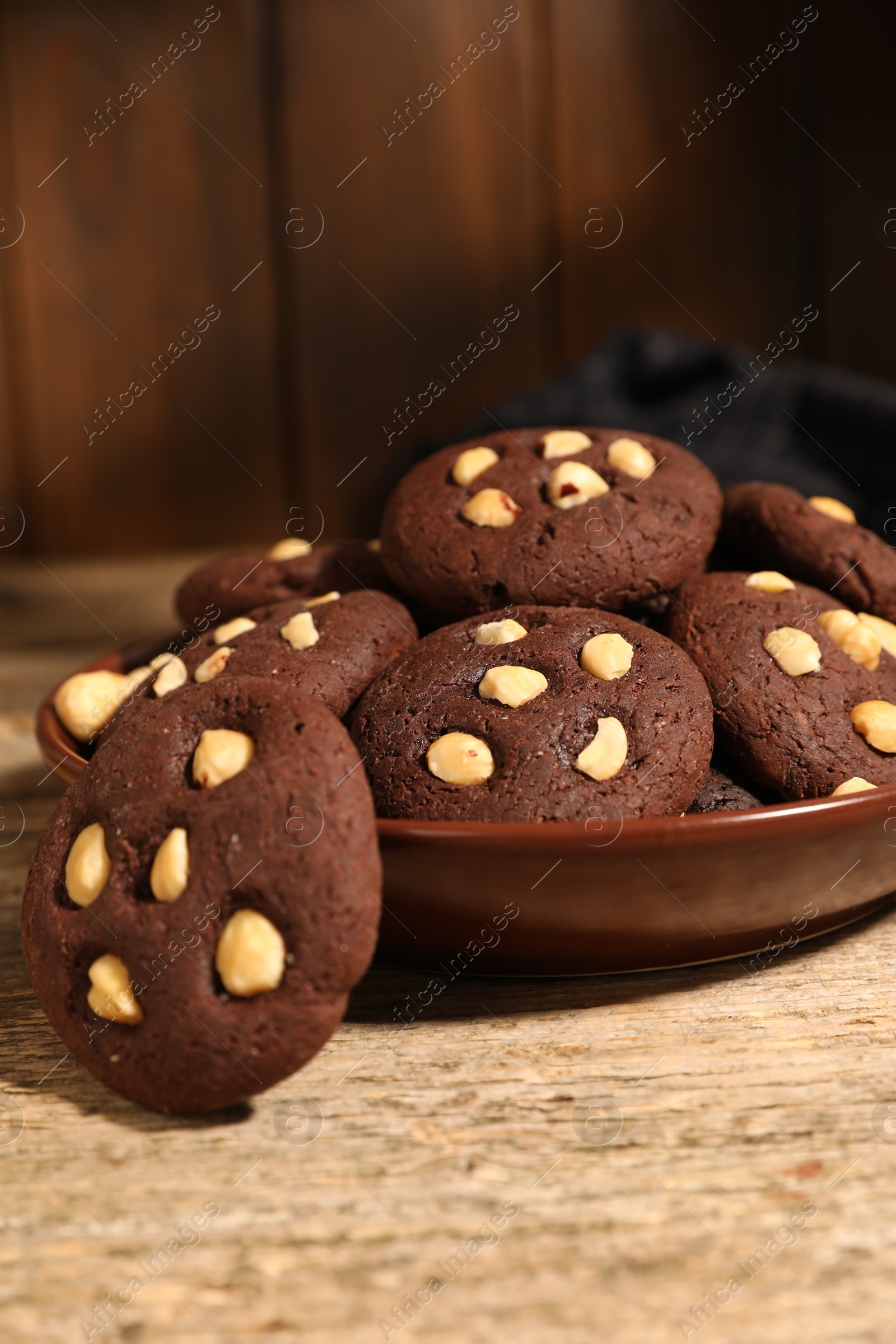 Photo of Tasty chocolate cookies with hazelnuts on wooden table, closeup