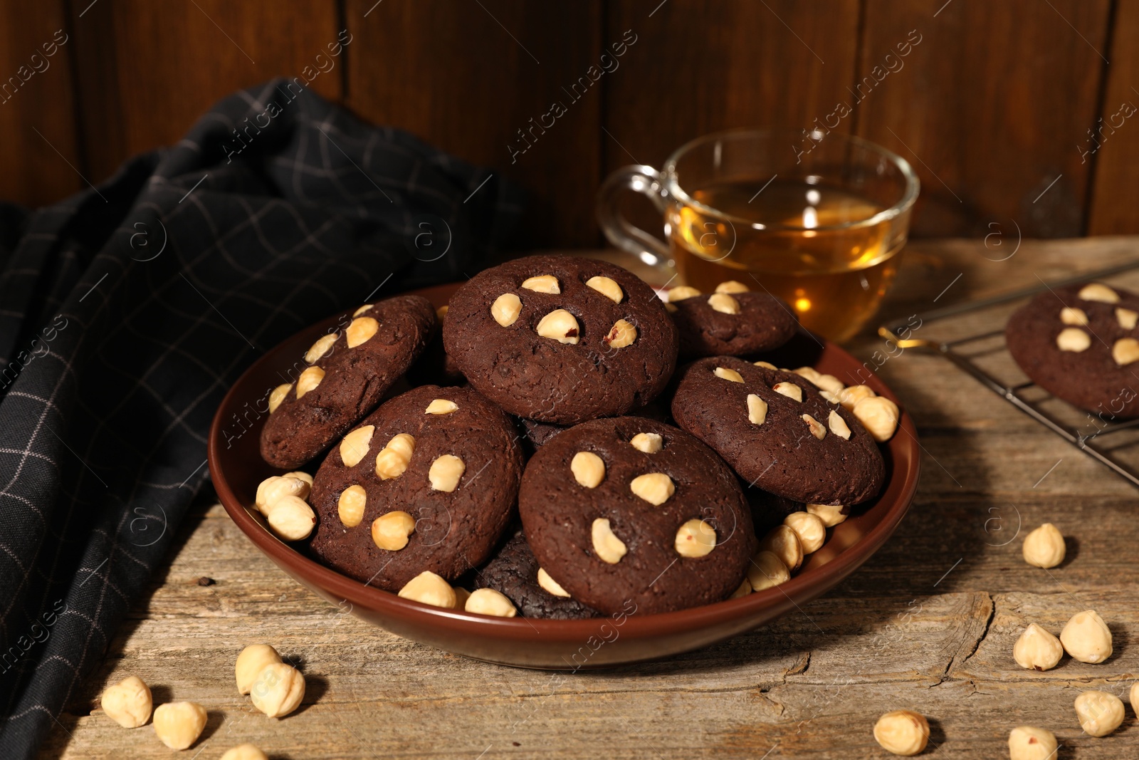 Photo of Tasty chocolate cookies with hazelnuts and tea on wooden table, closeup