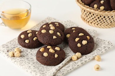 Photo of Tasty chocolate cookies with hazelnuts and tea on white table, closeup