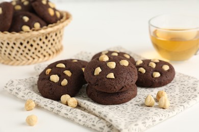 Photo of Tasty chocolate cookies with hazelnuts and tea on white table, closeup